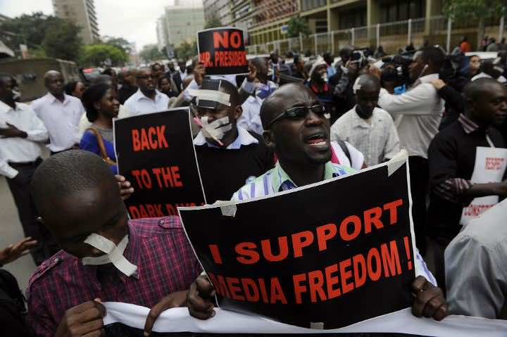Kenyan journalists, some covering their mouths with tape, hold signs during a protest against a controversial bill
