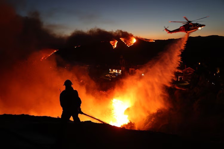 Firefighters attempting to control the blaze while a helicopter drops water on fire ravaged Pacific Palisades in Califortinia.&nbsp; Photo credit: David Swanson/AFP