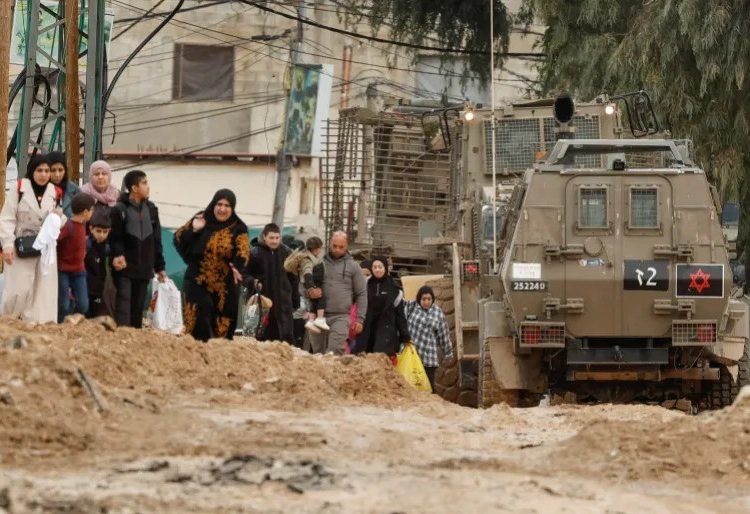 Palestinians leaving Jenin camp during an Israeli raid as they walk past an Israeli military vehicle. Raneen Sawafta/Reuters