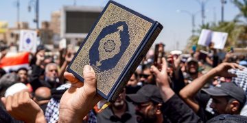 A demonstrator holds a copy of the Quran during a rally denouncing the burning of the Quran in Sweden in Iraq's central shrine city of Kufa east of nearby Najaf on July 21