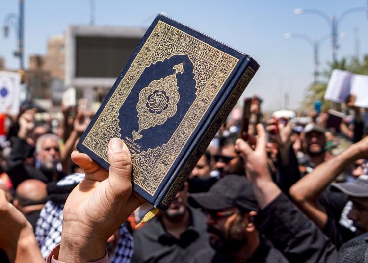A demonstrator holds a copy of the Quran during a rally denouncing the burning of the Quran in Sweden in Iraq's central shrine city of Kufa east of nearby Najaf on July 21