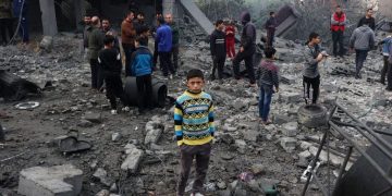 Palestinian child standing on the backdrop of destroyed buldings from Israeli attacks