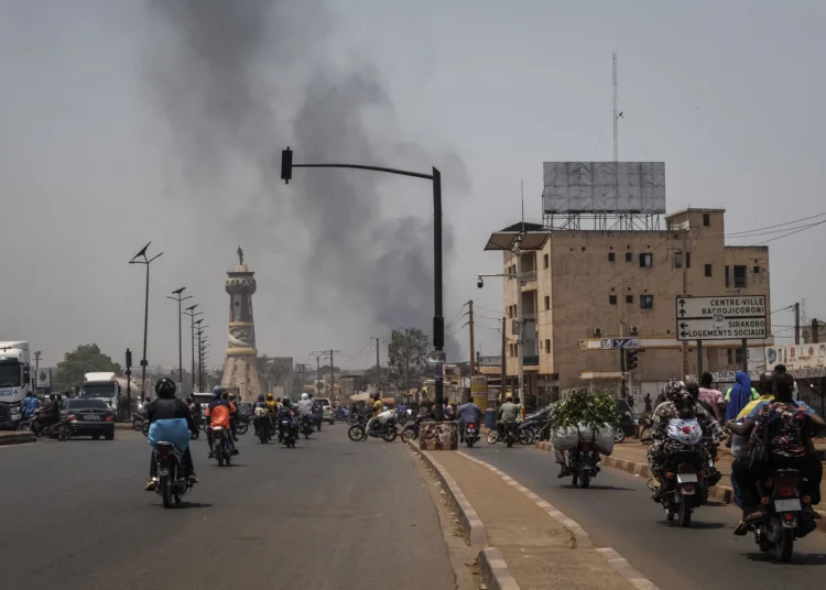 A column of black smoke rises above the buildings as traffic passes in front of the Tour de l'Afrique monument in Bamako on April 26, 2026. Photograph by AFP.