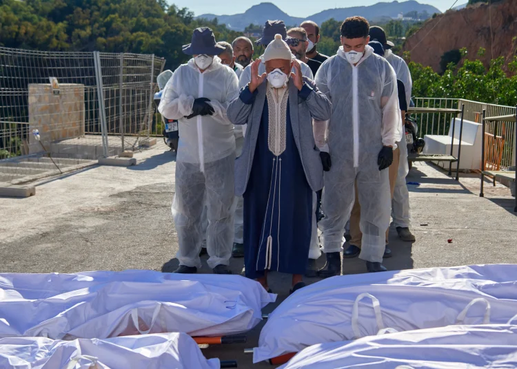 A man, accompanied by funeral workers, prays over the bodies of migrants who died while trying to cross from Morocco to Ceuta, on 21 August 2026. AP/Antonio Sempere