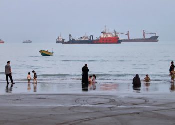 People spend time at a beach as commercial vessels are anchored in the Strait of Hormuz off Bandar Abbas, Iran, Wednesday, Aug. 5, 2026. (Amirhosein Khorgooi/ISNA via AP)