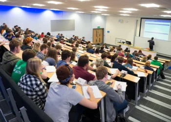 Students attend a lecture in a university auditorium as an instructor delivers a presentation at the front of the classroom.