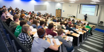 Students attend a lecture in a university auditorium as an instructor delivers a presentation at the front of the classroom.