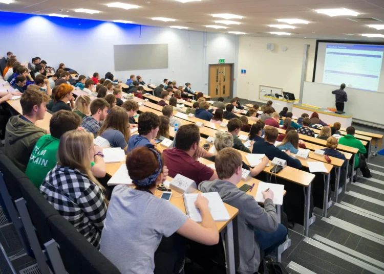 Students attend a lecture in a university auditorium as an instructor delivers a presentation at the front of the classroom.