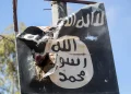 A torn ISIS flag hangs from a damaged structure.