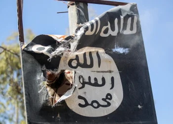 A torn ISIS flag hangs from a damaged structure.
