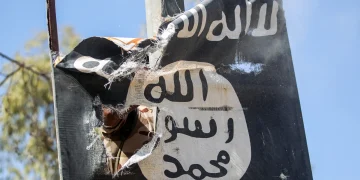 A torn ISIS flag hangs from a damaged structure.