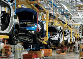 Workers assemble vehicles along an automotive production line at a manufacturing plant.