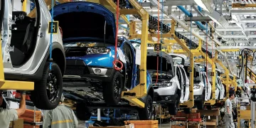 Workers assemble vehicles along an automotive production line at a manufacturing plant.