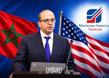 US-based Moroccan journalist Mohamed El Hajjam speaking at a podium, with Moroccan and American flags and the Moroccan American Network logo in the background. (Designed by MWN team)