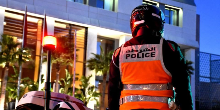 A Moroccan police officer stands beside a police motorcycle during an evening security operation.