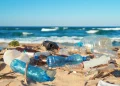 Plastic bottles and other waste litter a sandy beach along the ocean.