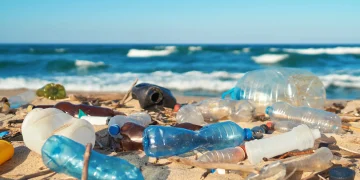 Plastic bottles and other waste litter a sandy beach along the ocean.