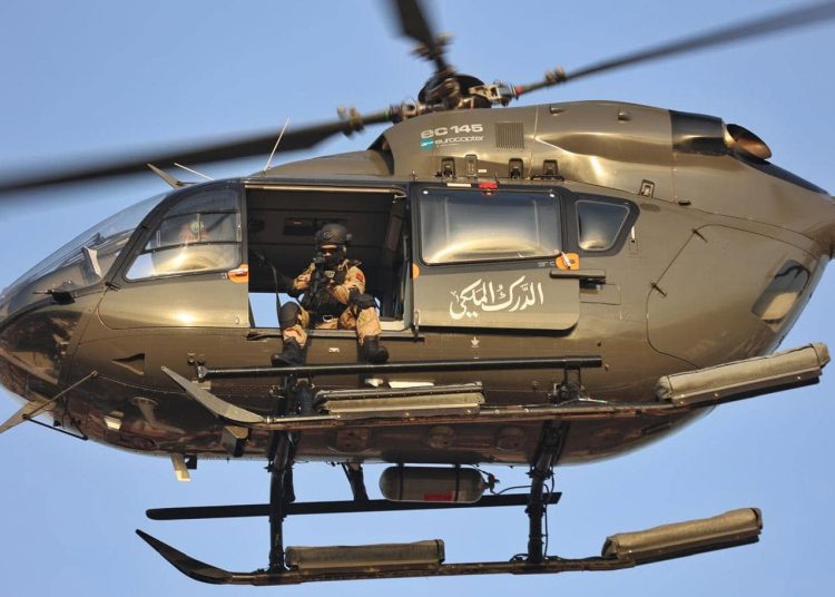 An armed member of Morocco’s Royal Gendarmerie sits at the open doorway of a Eurocopter EC145 helicopter in flight.
