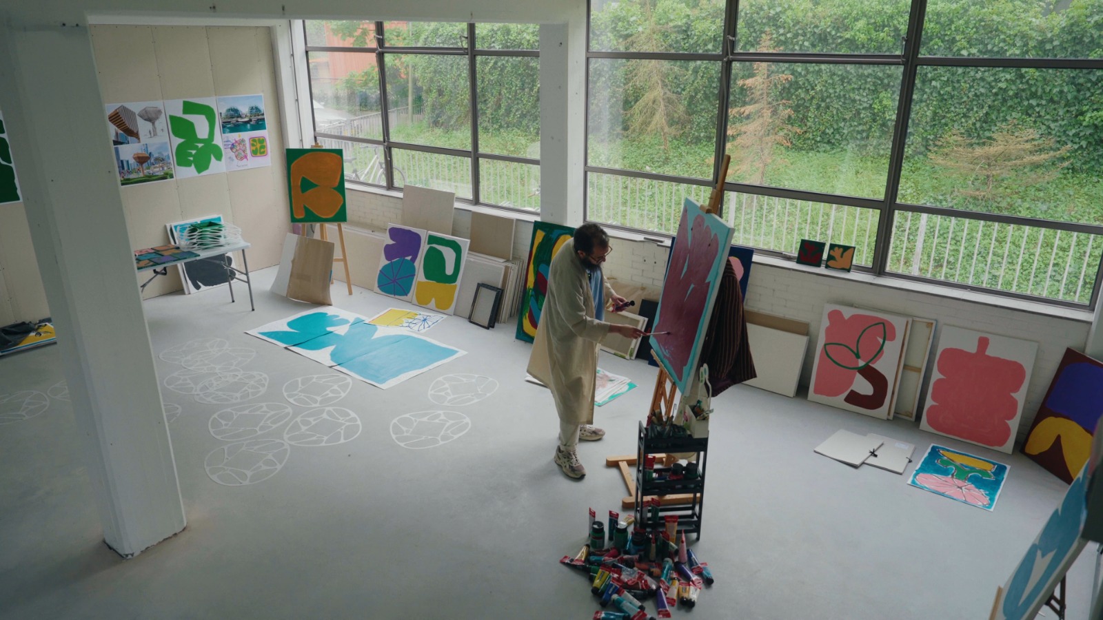 A photo of Moroccan-Dutch artist Hakim El Amrani painting in his studio, surrounded by colorful abstract artworks.